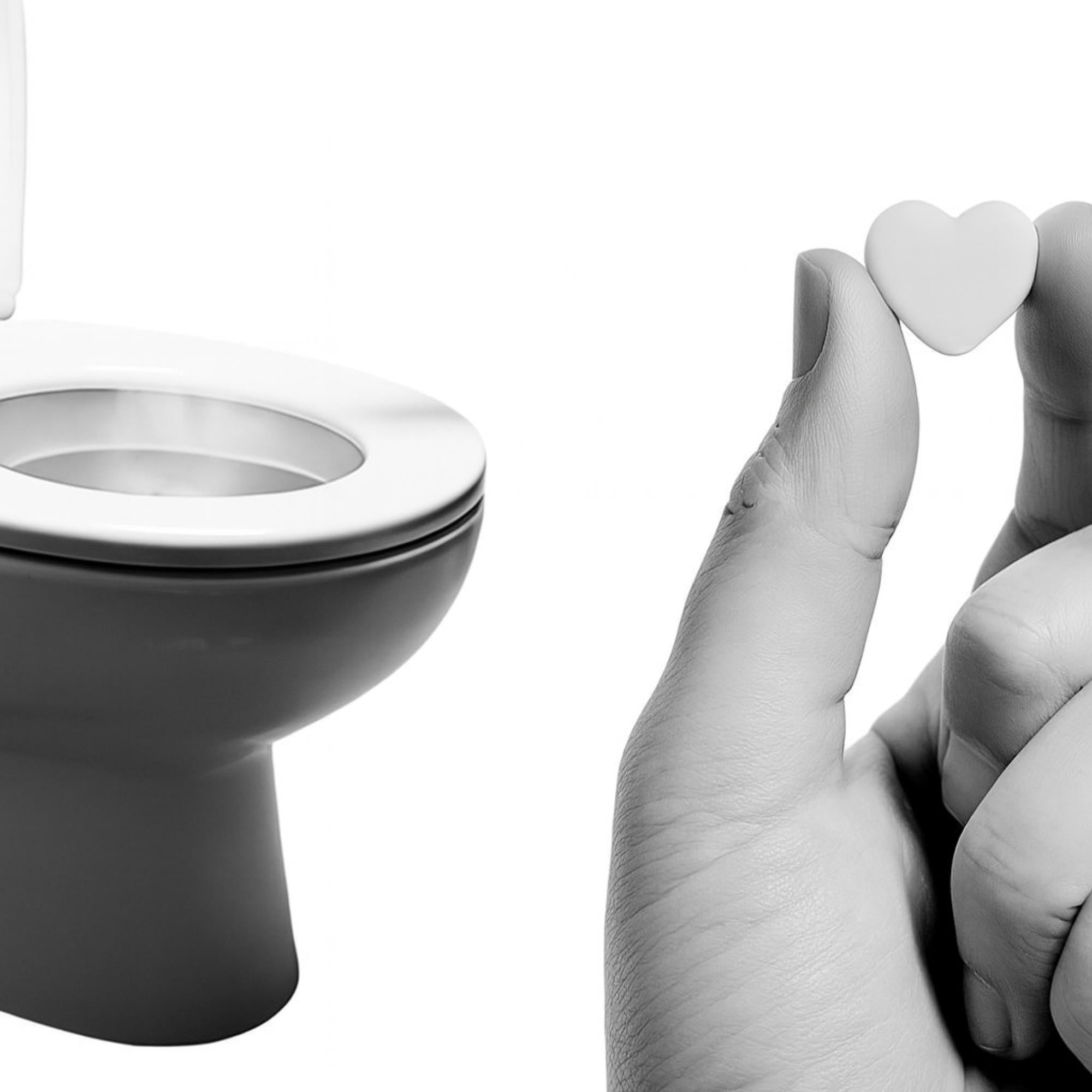White heart-shaped object held by a hand next to a toilet.